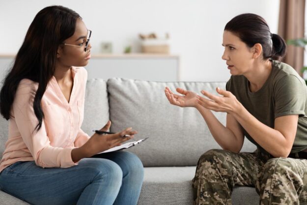 A therapist is helping a veteran with PTSD. They are sitting together on a couch.