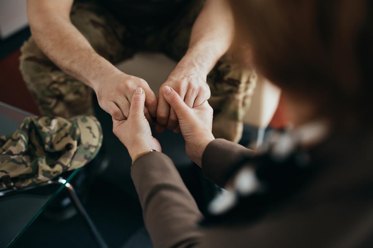 A veteran struggling with depression sits across from a professional counselor while holding hands.